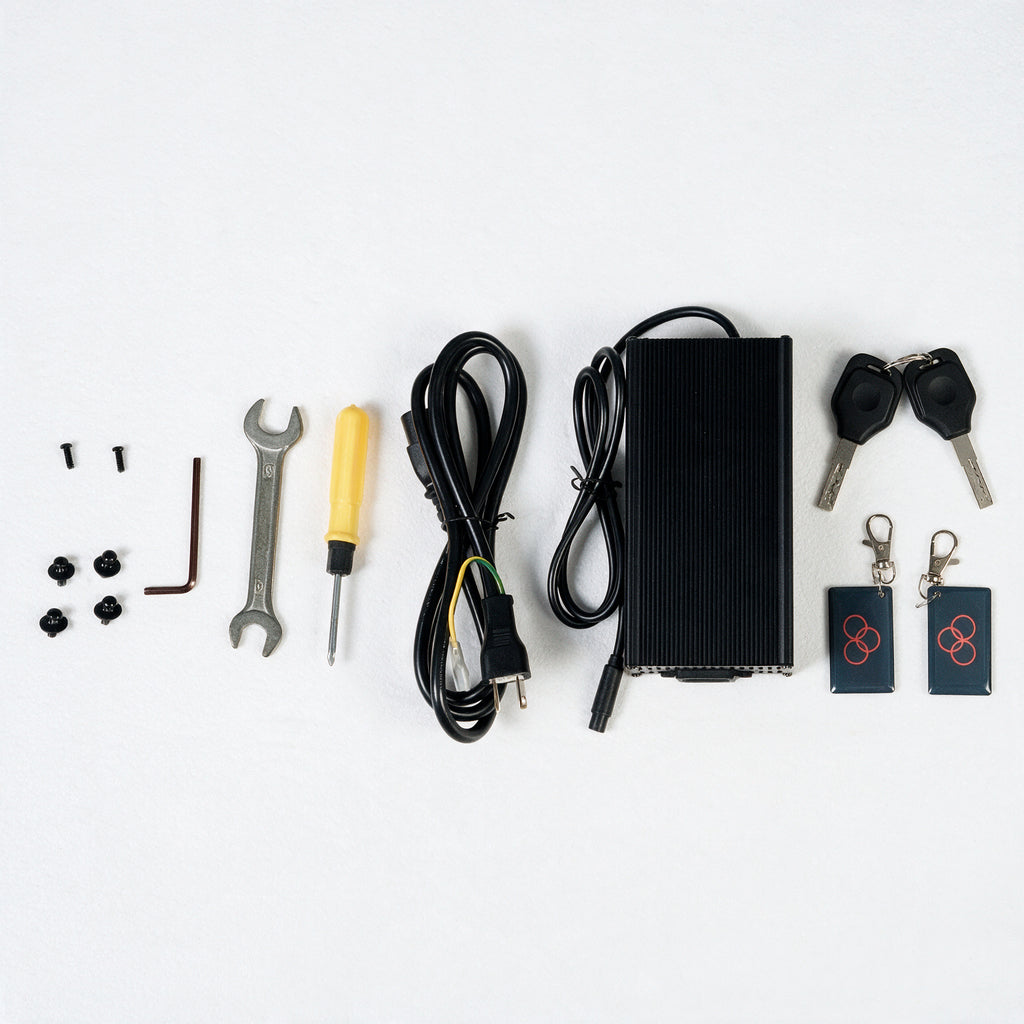 A flat-lay view of an electric scooter remote control kit on a white background, including a black control box, cables, two key fobs, two keys, a wrench, a screwdriver, and mounting screws.