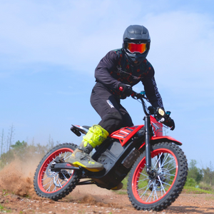 Person riding Ainohot velox dirt bike on a dirt track with a clear blue sky.