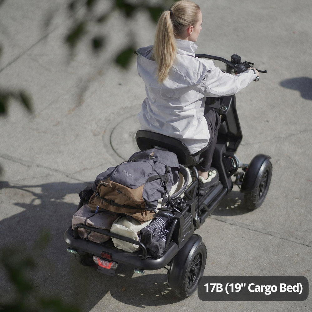 A woman rides a black four-wheeled electric cargo scooter on a concrete surface, viewed from behind. The scooter has a rear cargo bed carrying a gray backpack and other gear.