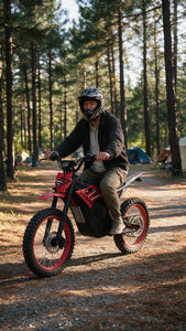 A person wearing a black helmet and dark jacket rides a red and black electric dirt bike on a forest path surrounded by tall pine trees.